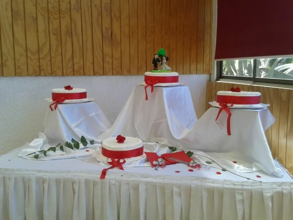 Cabaña blanca con techo rojo rodeada de árboles y jardín verde del complejo