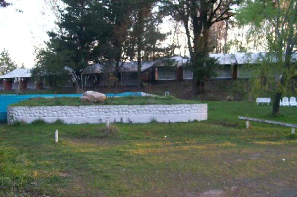 Área verde del complejo con hotel al fondo y sillas blancas en el jardín